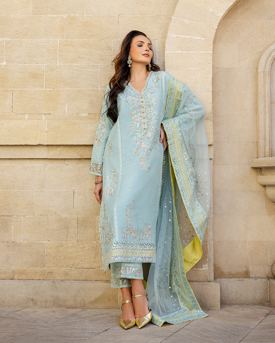 Woman leaning against sandstone wall wearing icy blue embroidered raw silk suit