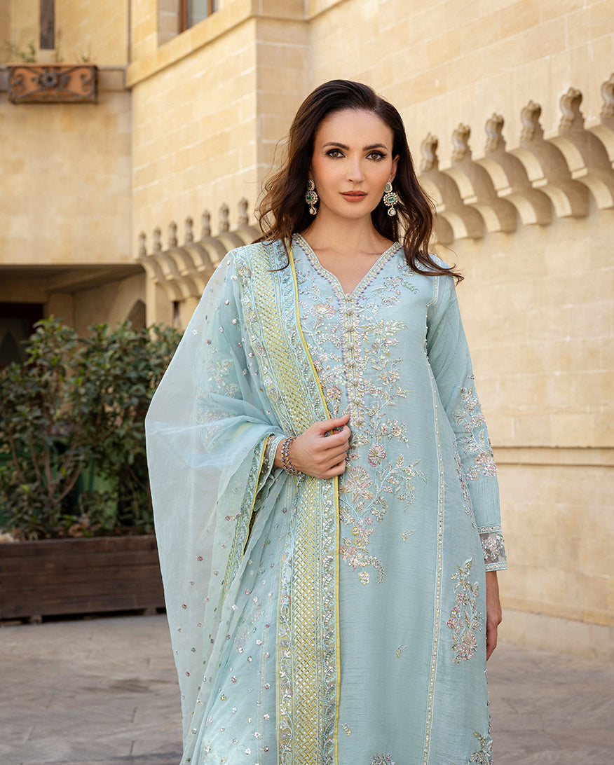 Woman wearing icy blue embroidered raw silk suit standing before arched sandstone wal