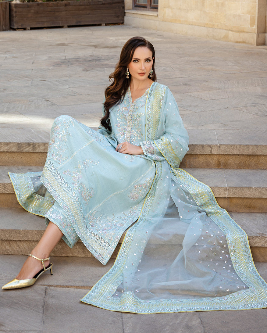 Woman seated on stone steps wearing icy blue raw silk suit with dupatta fanned out