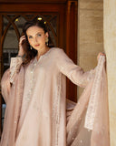 Woman leaning against stone pillar wearing rose beige raw silk suit with embroidered dupatta