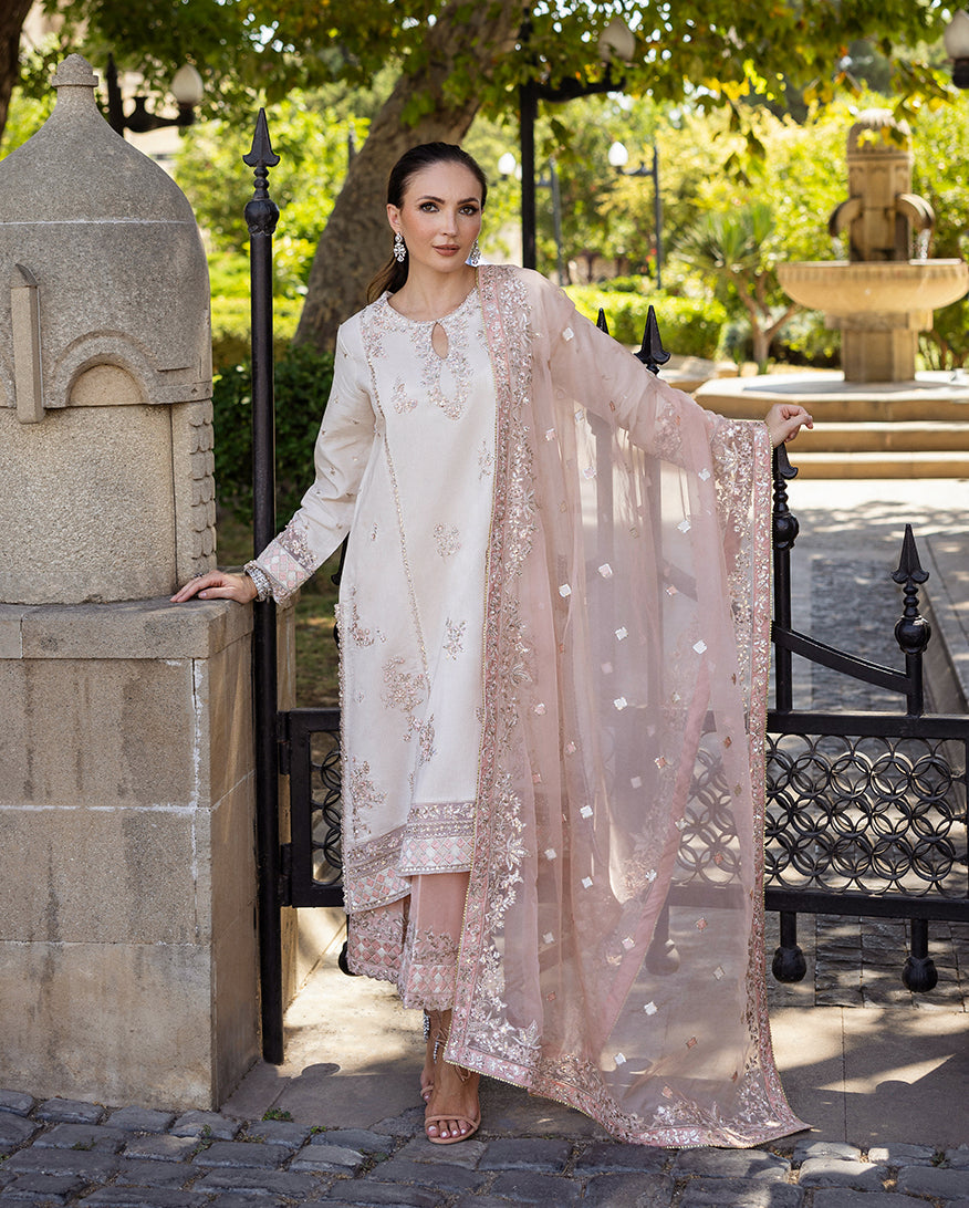 Woman wearing Astrid Bloom off white embroidered raw silk suit with pink organza dupatta at garden gate