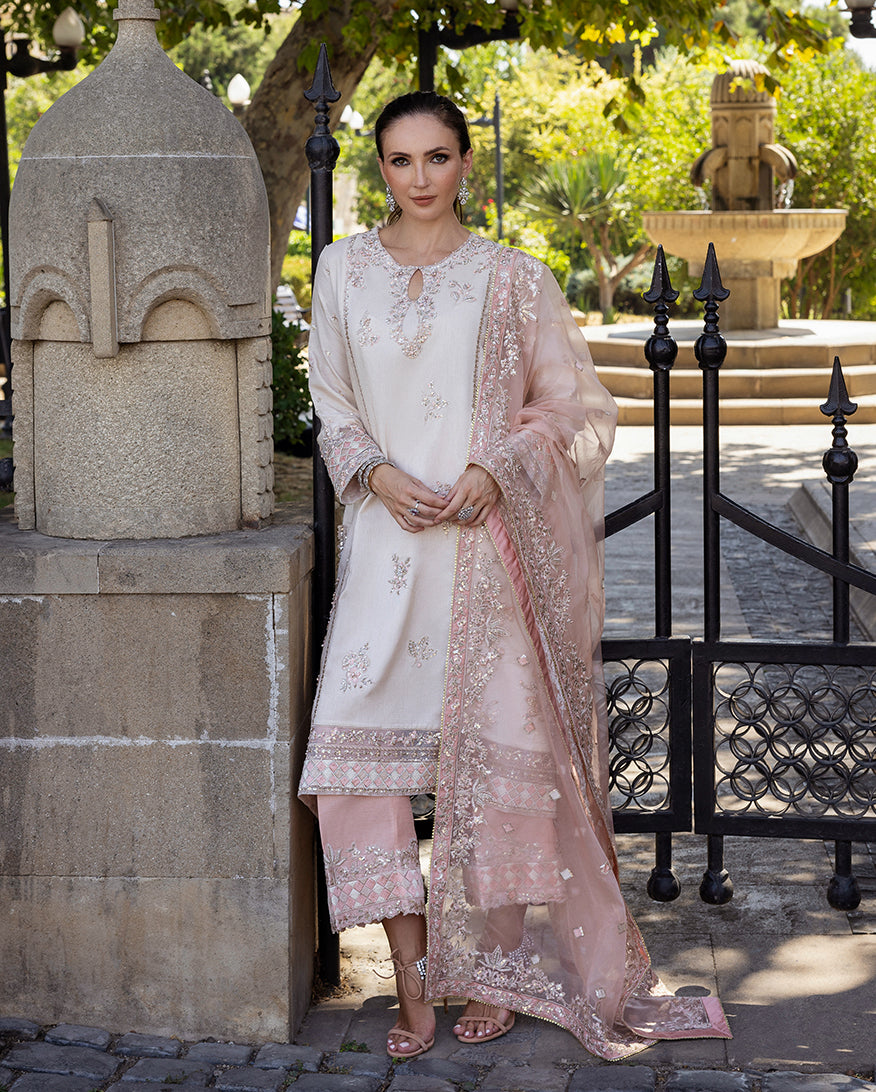 Woman wearing Astrid Bloom off white embroidered raw silk suit with pink organza dupatta at garden gate
