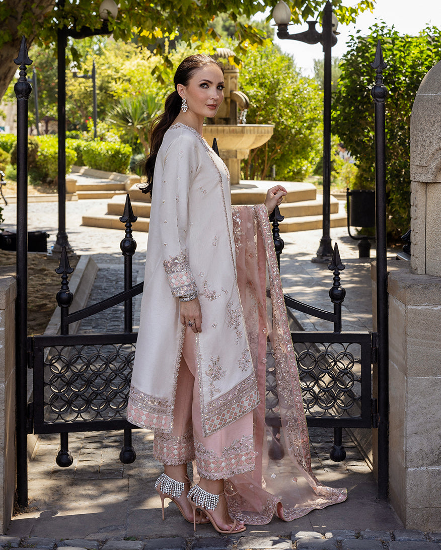 Woman wearing Astrid Bloom off white embroidered raw silk suit with pink organza dupatta at garden gate