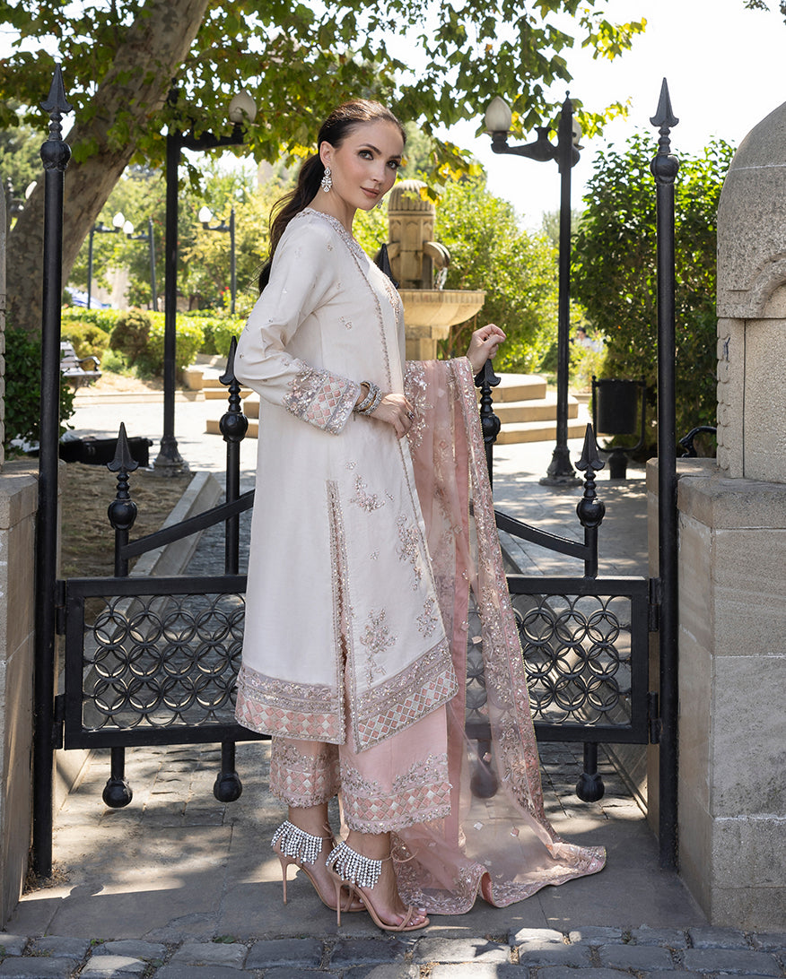 Woman wearing Astrid Bloom off white embroidered raw silk suit with pink organza dupatta at garden gate