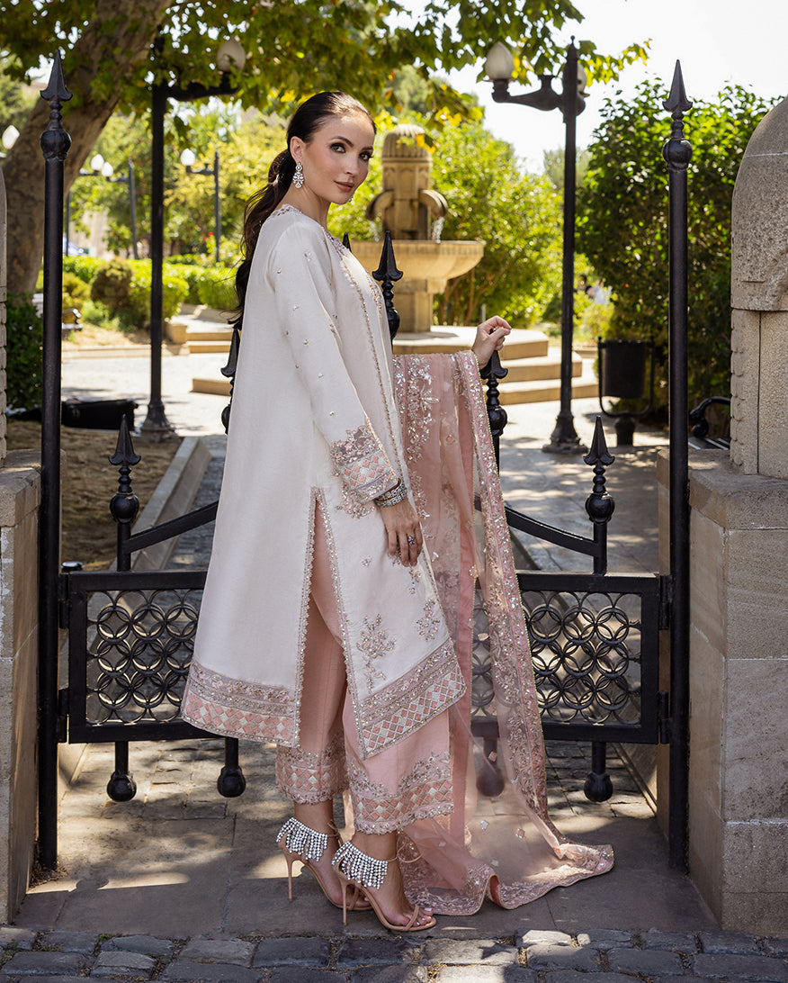 Woman wearing Astrid Bloom off white embroidered raw silk suit with pink organza dupatta at garden gate