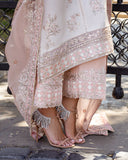 Woman wearing Astrid Bloom off white embroidered raw silk suit with pink organza dupatta at garden gate