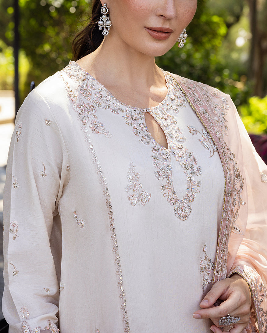 Woman wearing Astrid Bloom off white embroidered raw silk suit with pink organza dupatta at garden gate