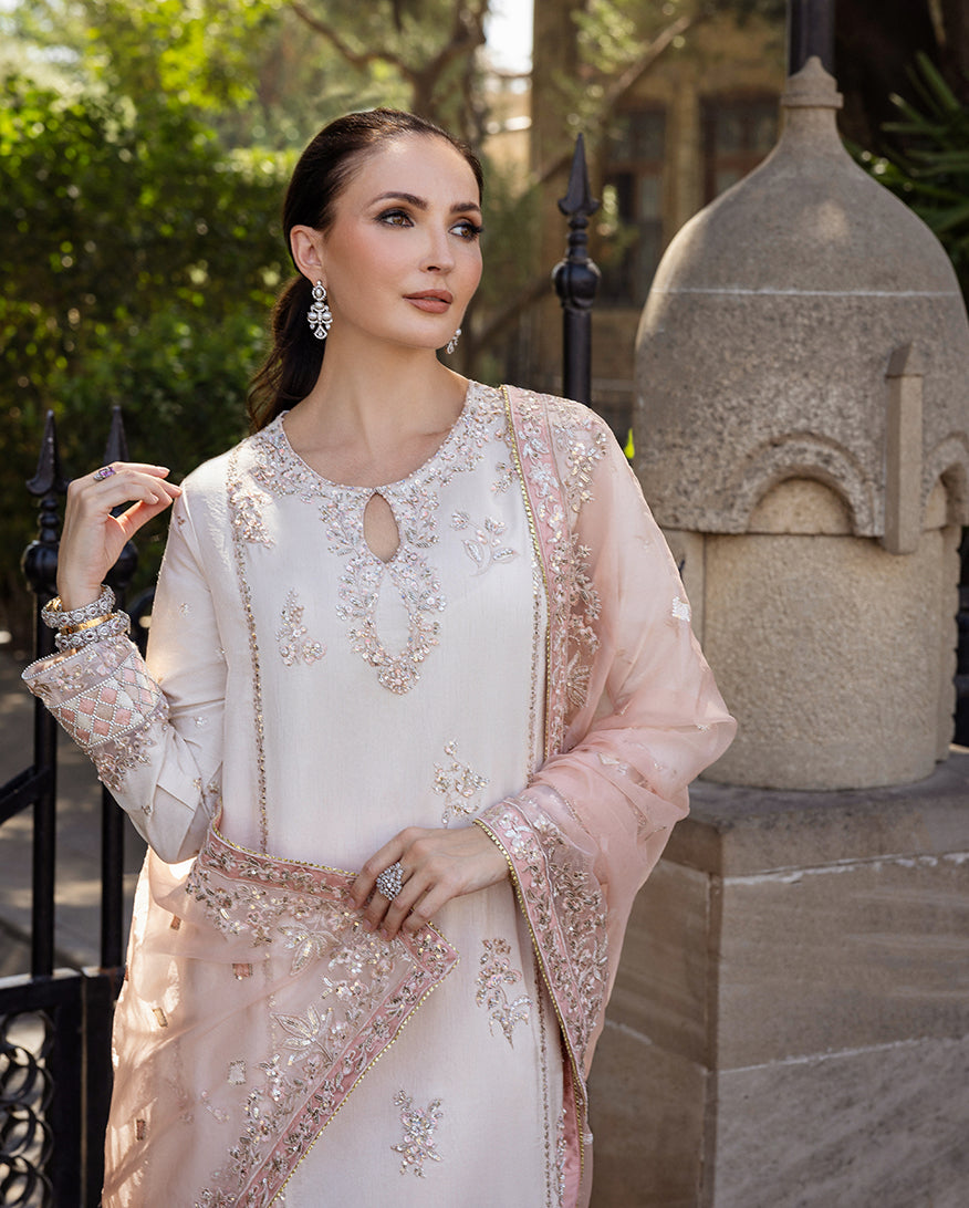 Woman wearing Astrid Bloom off white embroidered raw silk suit with pink organza dupatta at garden gate
