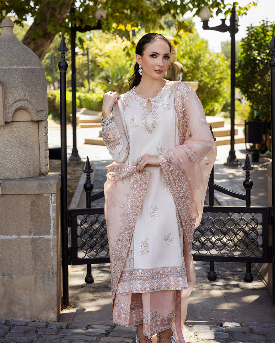 Woman wearing Astrid Bloom off white embroidered raw silk suit with pink organza dupatta at garden gate