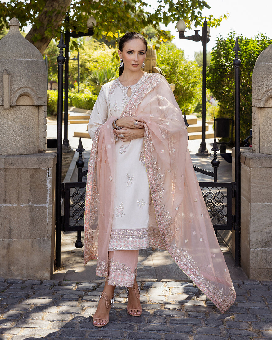 Woman wearing Astrid Bloom off white embroidered raw silk suit with pink organza dupatta at garden gate