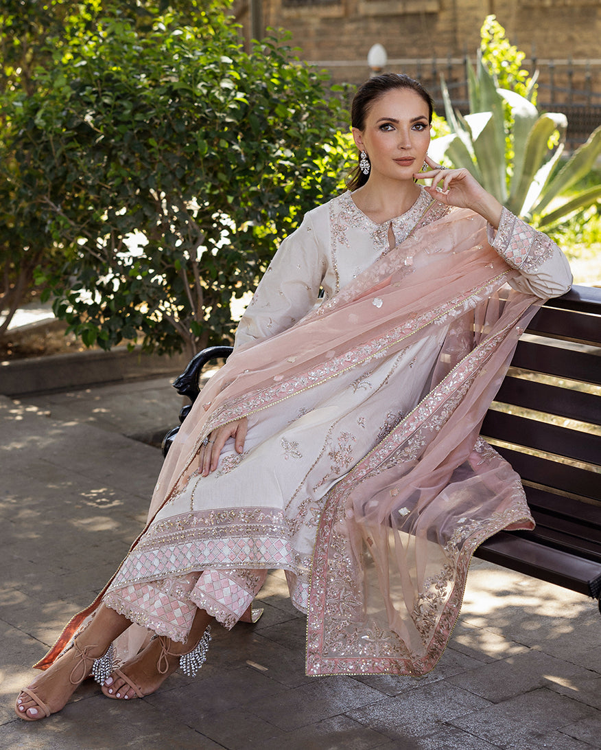 Woman wearing Astrid Bloom off white embroidered raw silk suit with pink organza dupatta at garden gate