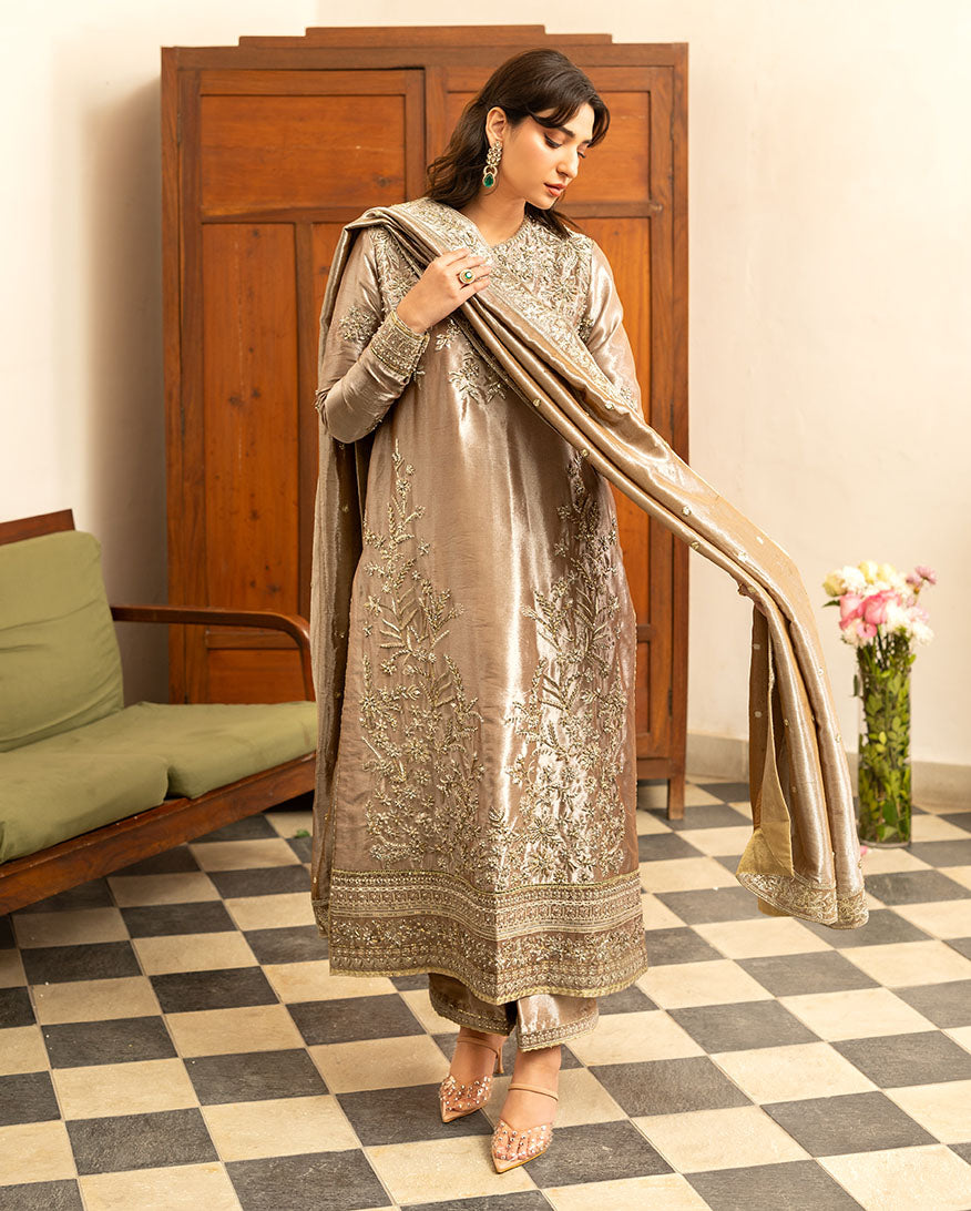 Woman wearing dark beige lama silk suit, front standing, adjusting dupatta, looking down