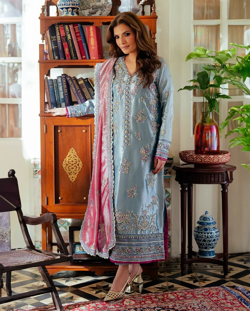 Woman wearing blue embellished satin zari suit, front standing by bookshelf