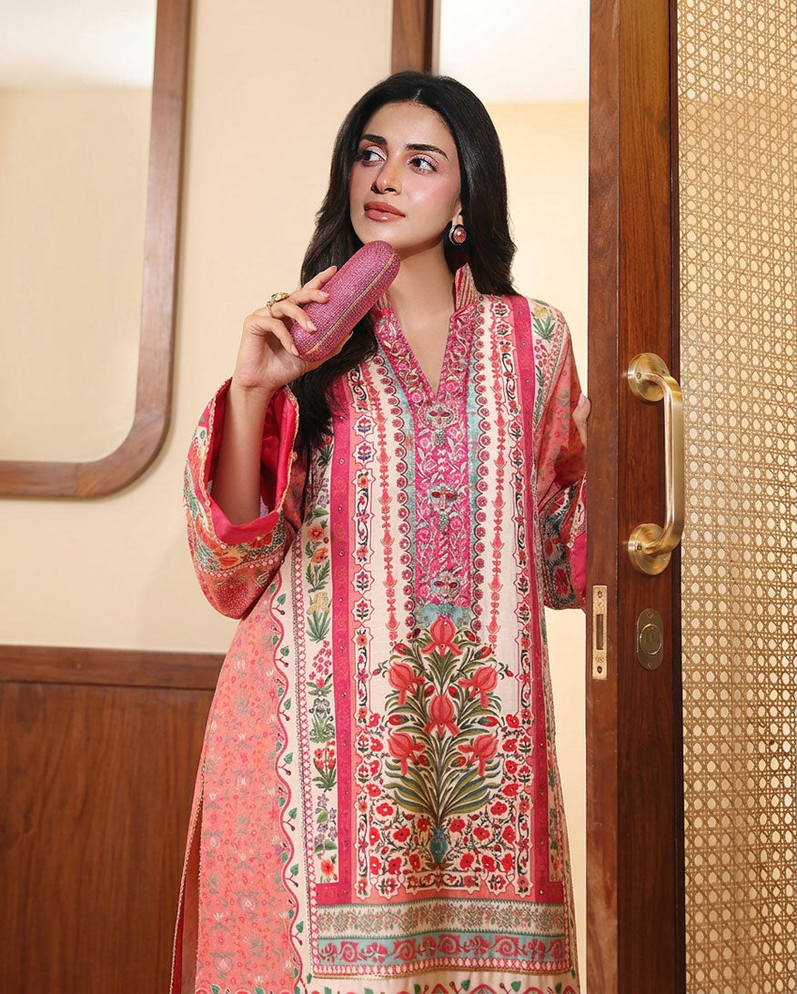 Woman wearing peach printed raw silk suit standing by a doorway, holding a clutch bag