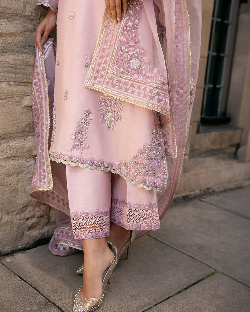 Woman in pink embroidered raw silk kurta with Swarovski crystal and tilla work, standing by stone window
