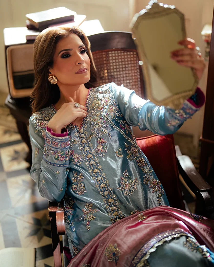 Woman wearing blue satin zari suit, seated, close-up styled pose holding mirror