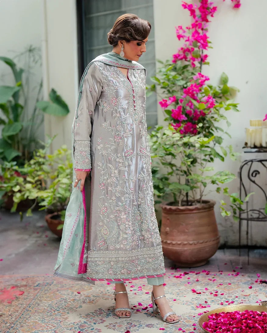 Woman wearing silver embellished satin zari suit, side standing, looking down