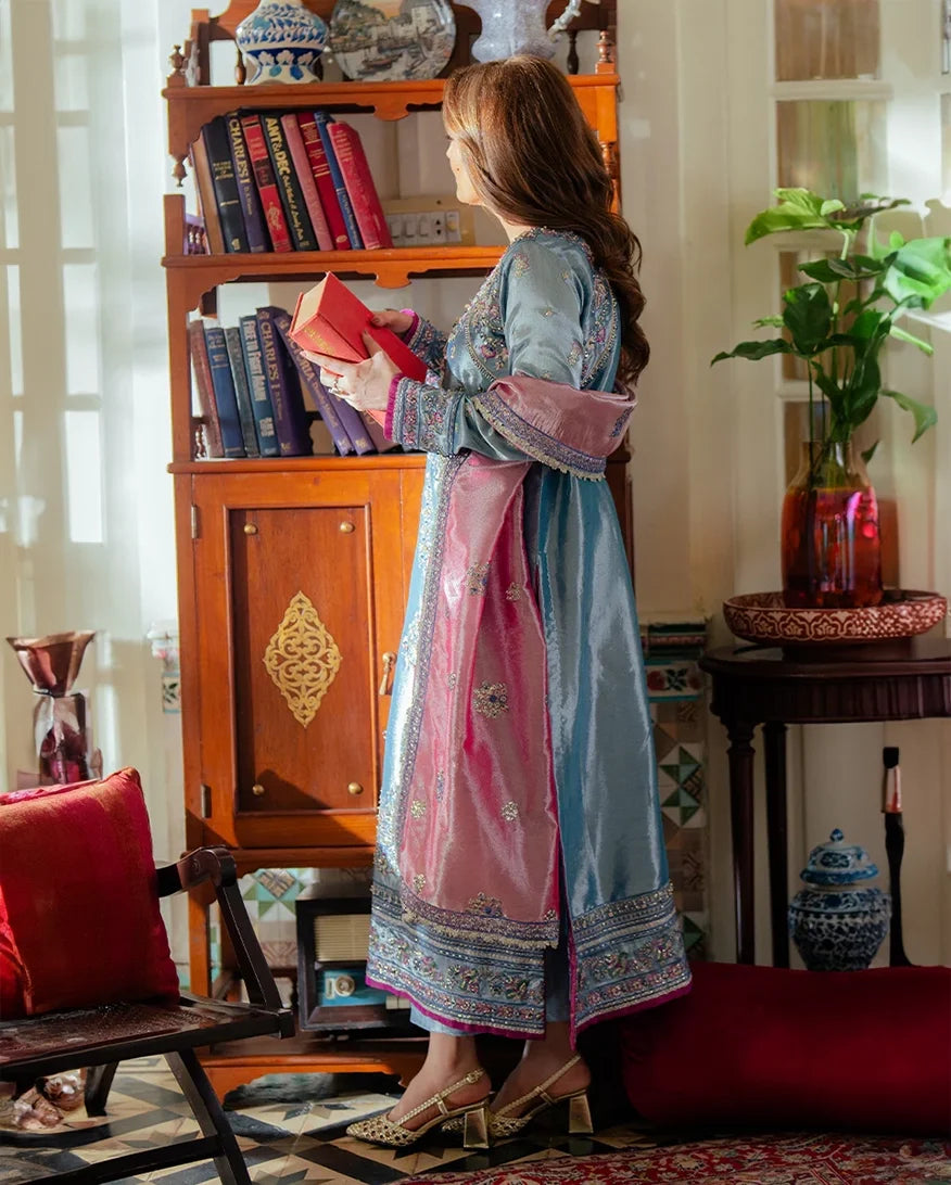 Woman wearing blue embellished satin zari suit, side standing, dupatta draped, holding a book