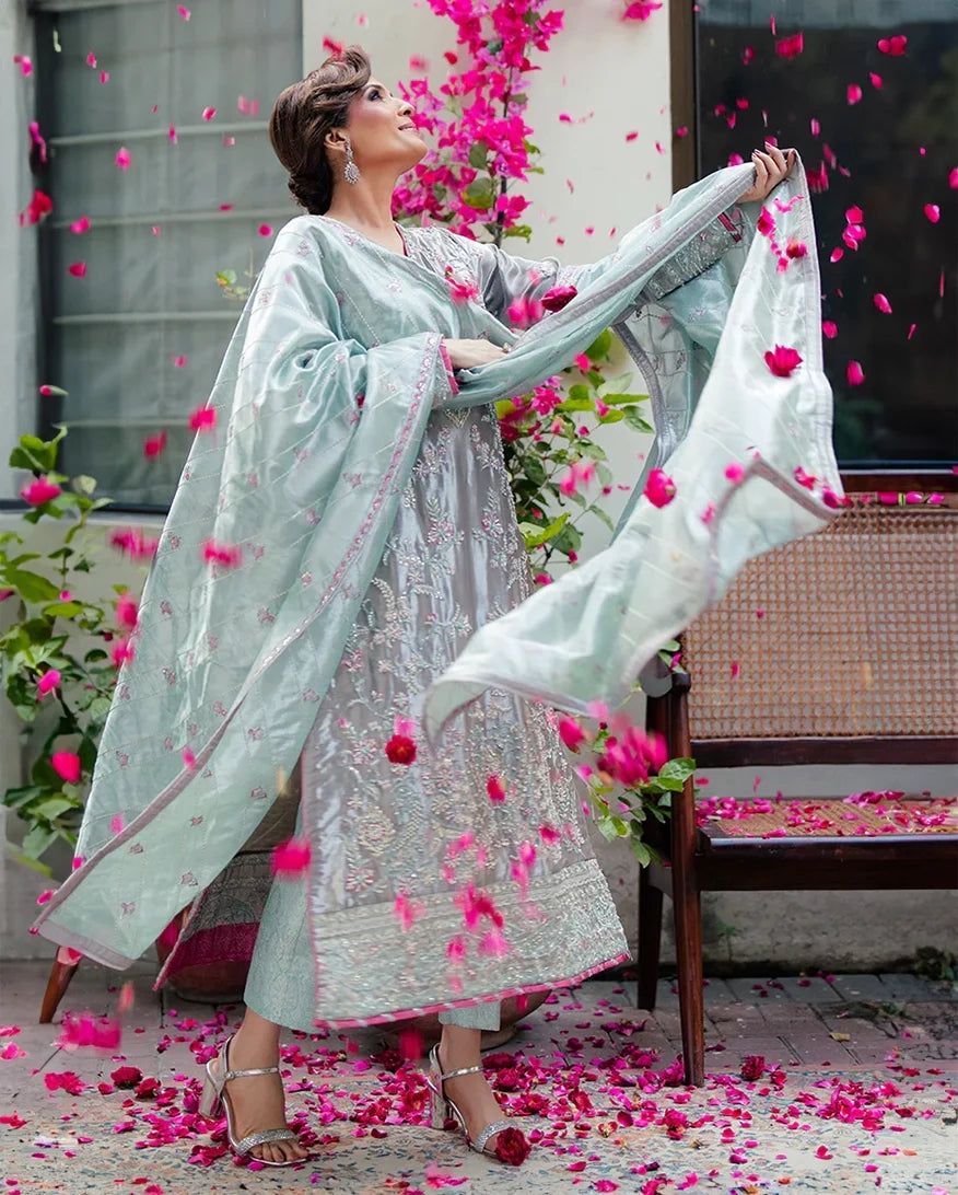 Woman wearing silver embellished satin zari suit, dupatta caught mid-air, rose petals falling