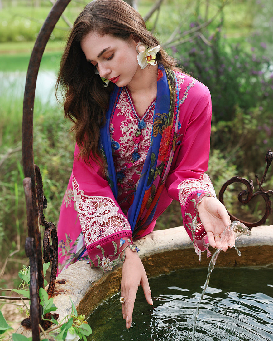 Woman touching water at stone basin, wearing fuchsia embroidered lawn collection suit with blue scarf and lace sleeve, Secret Garden collection