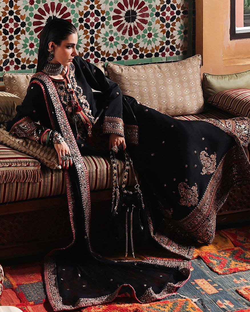 Woman wearing black raw silk suit seated with embroidered chiffon dupatta and sequinned daman border
