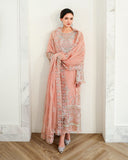 Woman wearing peach pink embellished organza suit, front standing, leaning against wall