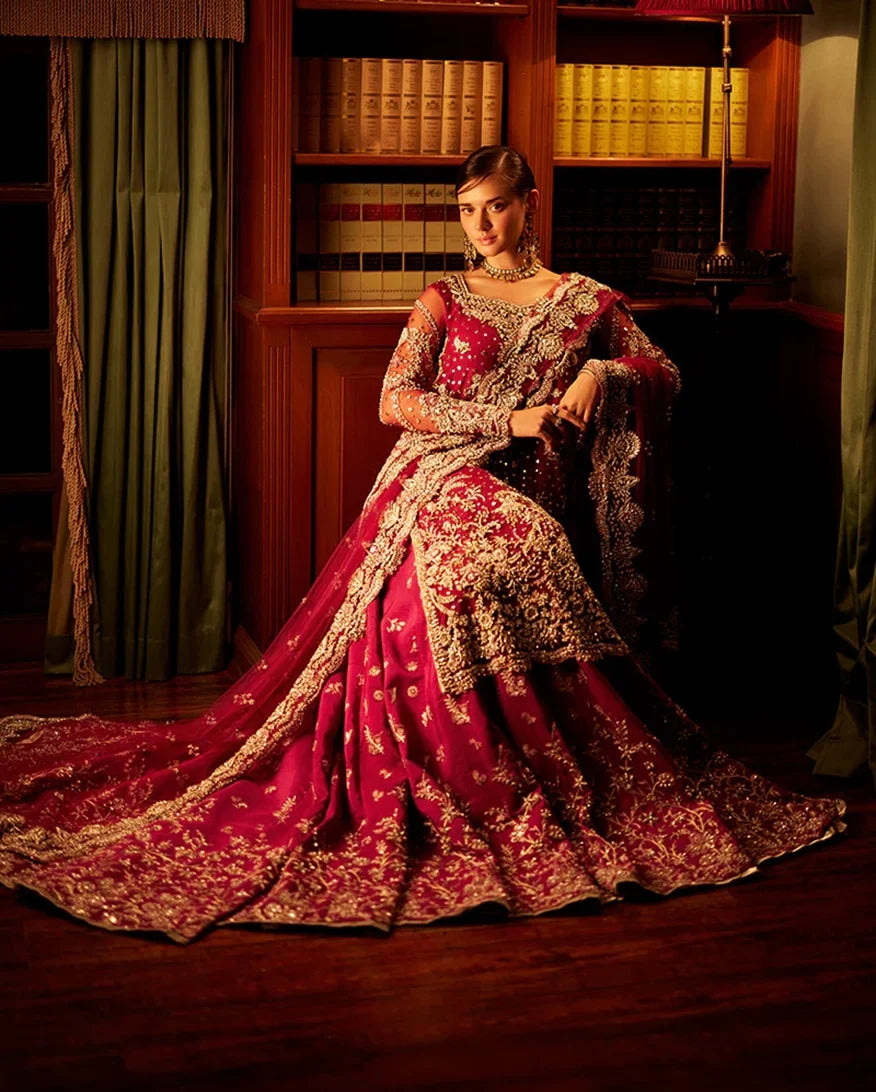 Woman wearing magenta embellished Net bridal lehenga, seated with dupatta draped over shoulder