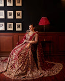 Woman wearing red embellished Net bridal gown with dupatta train, seated pose