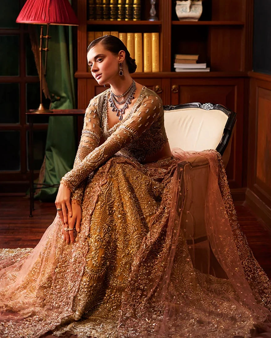 Bride seated in gold embellished lehenga with blush dupatta train draped over the chair