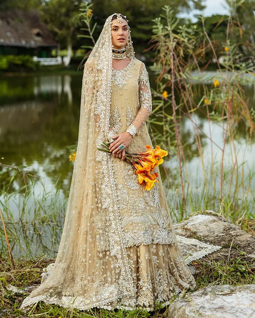 Woman wearing beige embellished Net bridal lehenga with sheer veil, holding orange bouquet