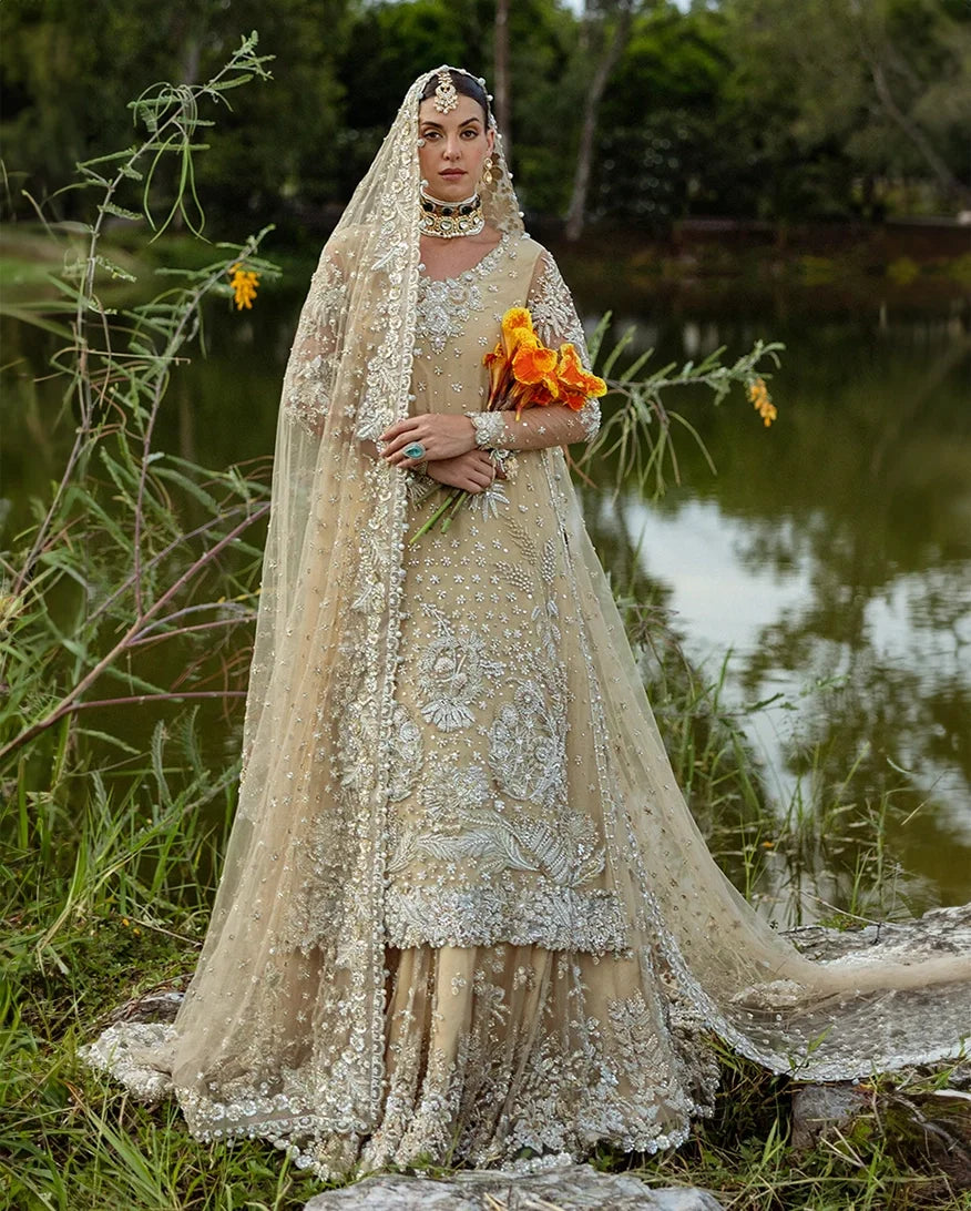 Woman wearing beige embellished Net bridal lehenga with sheer veil, holding bouquet