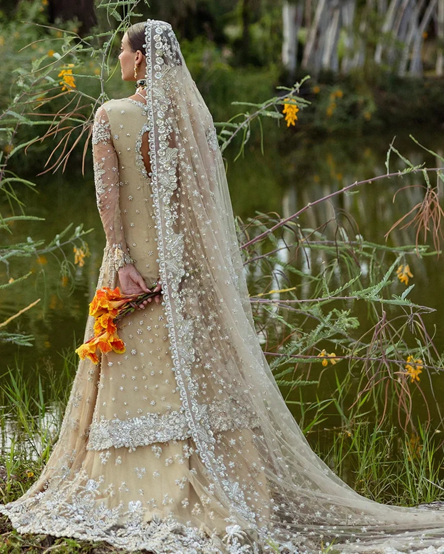 Back view of woman wearing beige embellished Net bridal lehenga with pearl-trimmed veil