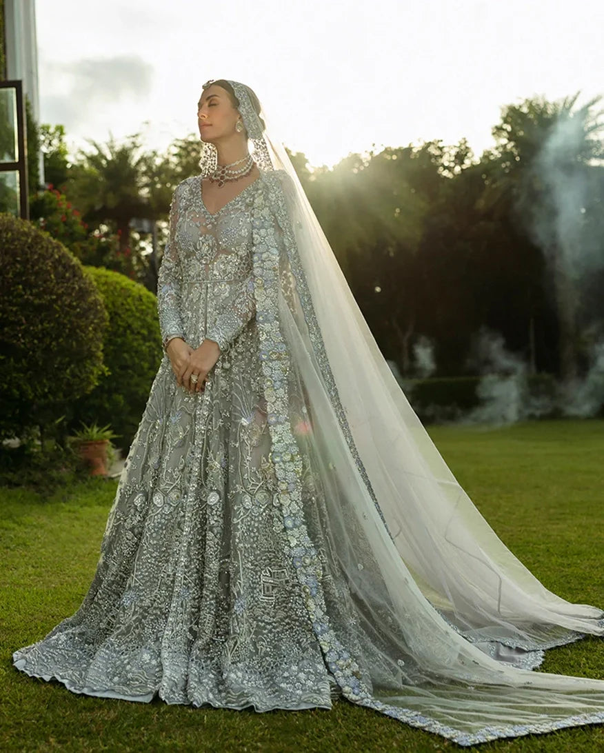 Woman in an Ice Blue Net bridal dress, embroidered dupatta trailing on grass, a Pakistani bridal wear design