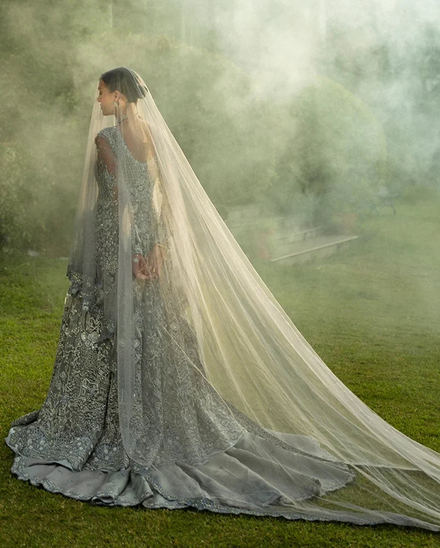 Woman in an Ice Blue Net bridal dress, back view with long embroidered veil, a bridal dress brand from Pakistan