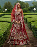 Woman wearing blood red embellished Net bridal lehenga with sheer veil, standing in garden