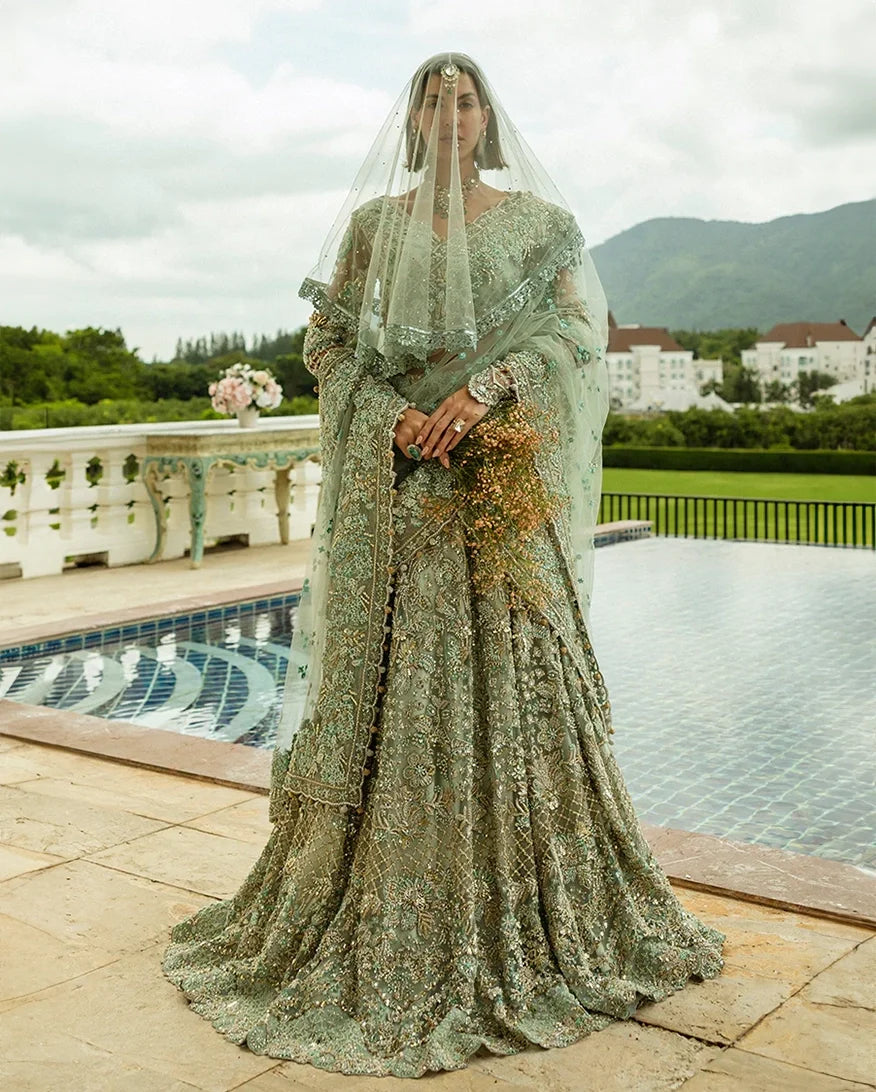 Woman wearing aqua green embellished Net bridal lehenga with sheer veil, holding bouquet