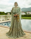 Woman wearing aqua green embellished Net bridal lehenga with sheer veil, holding bouquet