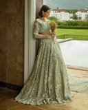 Woman wearing aqua green embellished Net bridal lehenga, leaning against pillar with bouquet