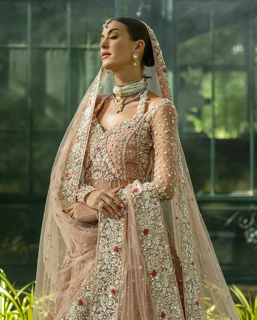 Woman wearing peach embellished Net bridal lehenga with sheer dupatta draped over head