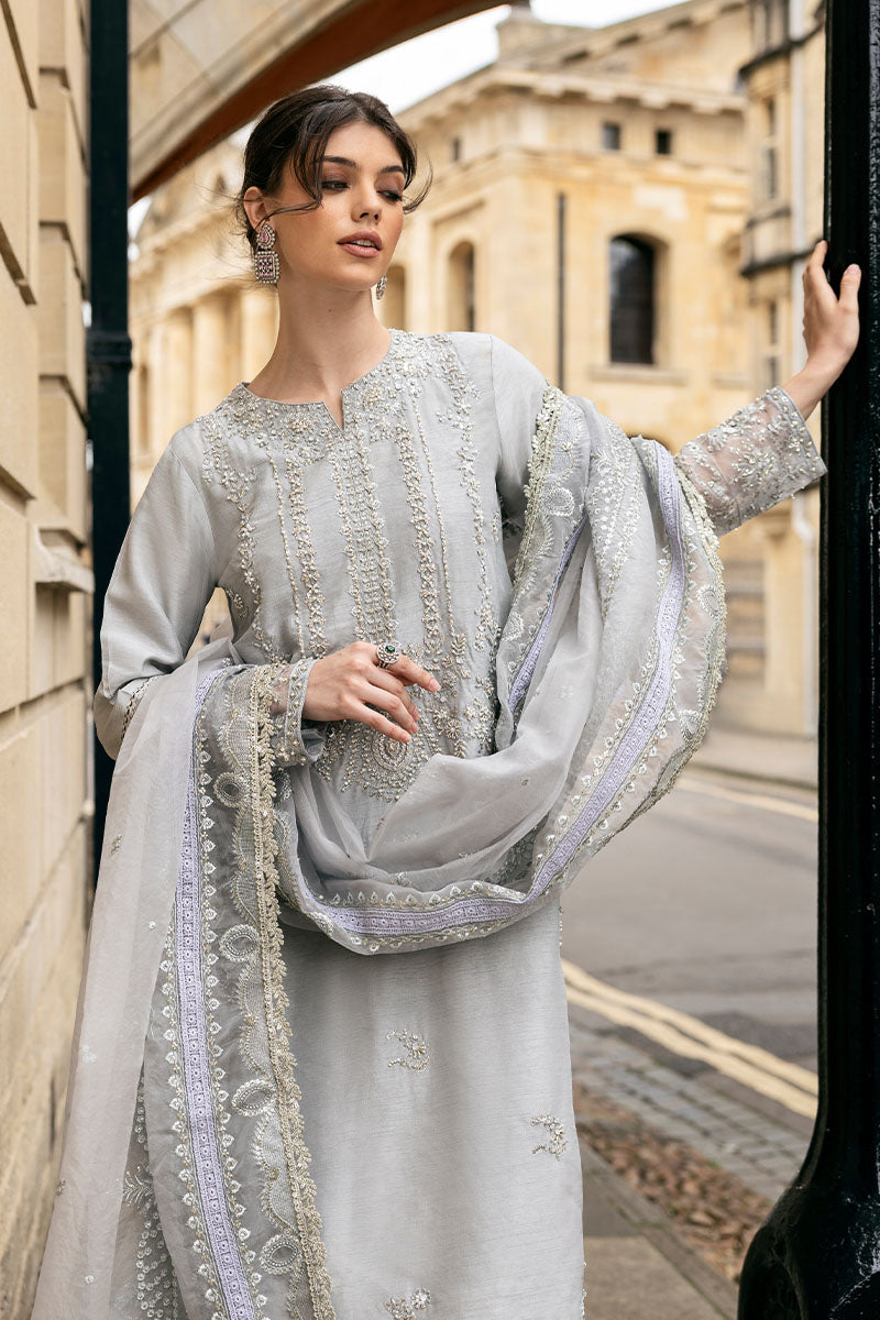 Woman wearing grey embroidered raw silk suit with diagonal color-blocked border under stone archway