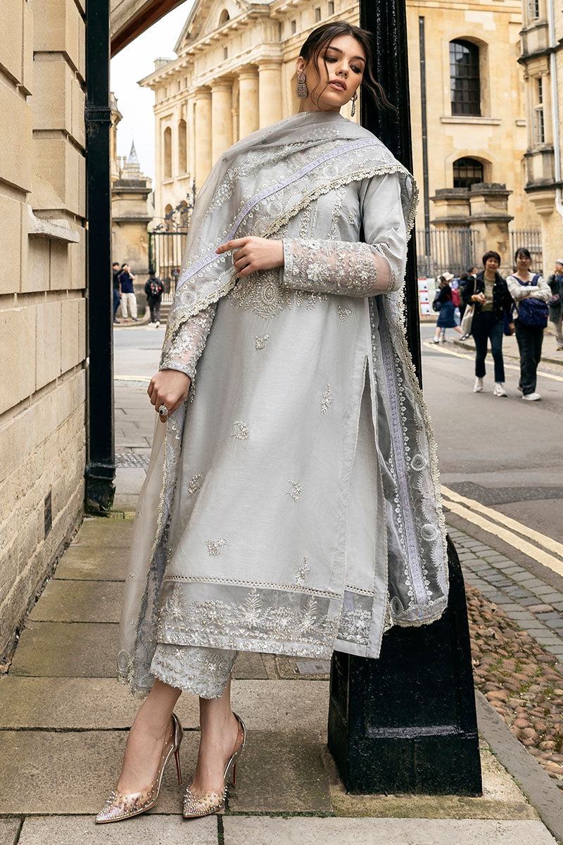Woman wearing grey embroidered raw silk suit with diagonal color-blocked border under stone archway