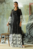 Woman wearing a Black embroidered Net suit with raw silk trousers, one hand resting on a wooden chair