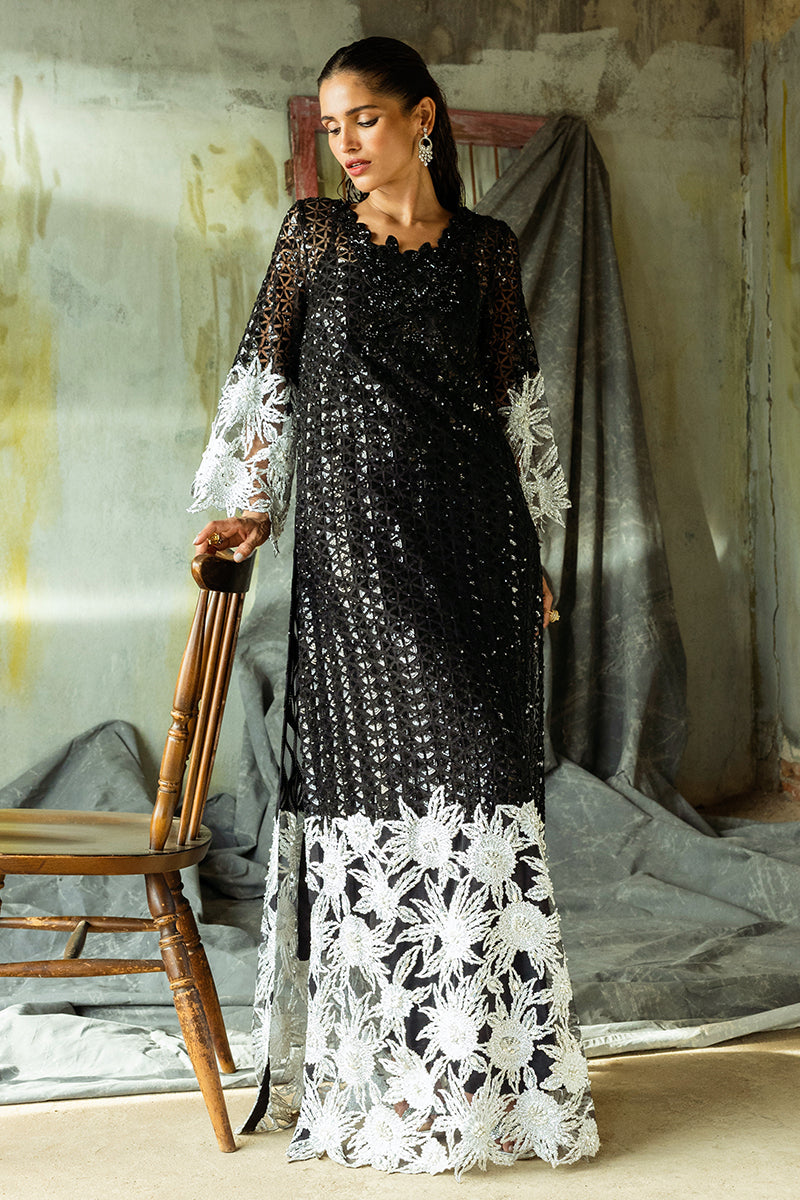 Woman wearing a Black Net suit, looking down at an embroidered floral hem