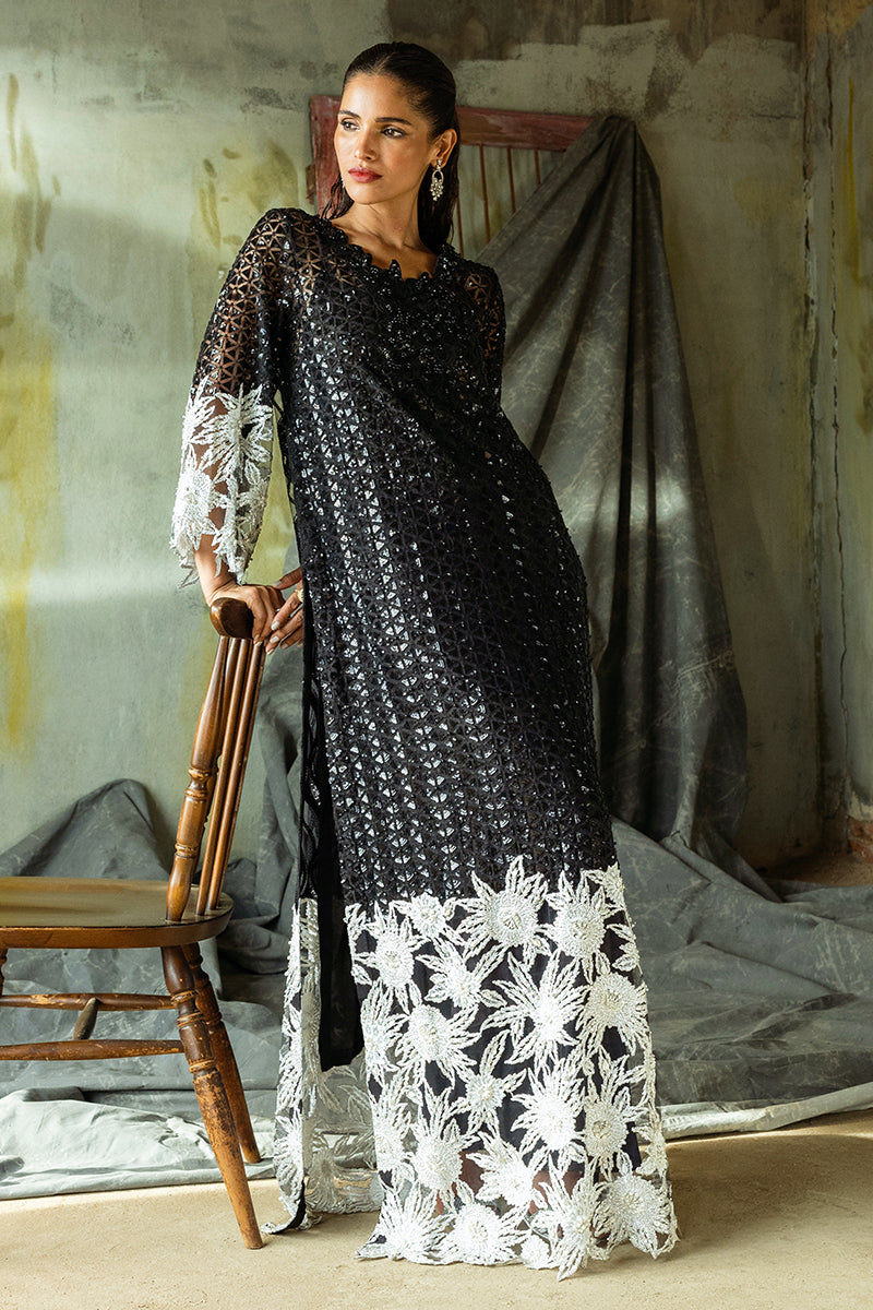 Woman wearing a Black embroidered Net suit, glancing to the side beside a wooden chair