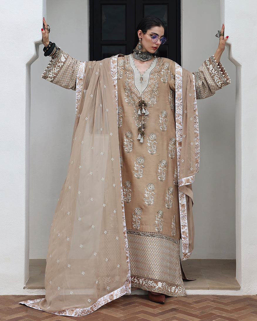 Woman wearing beige raw silk dress with dupatta draped and hand embellished silk sleeve balls