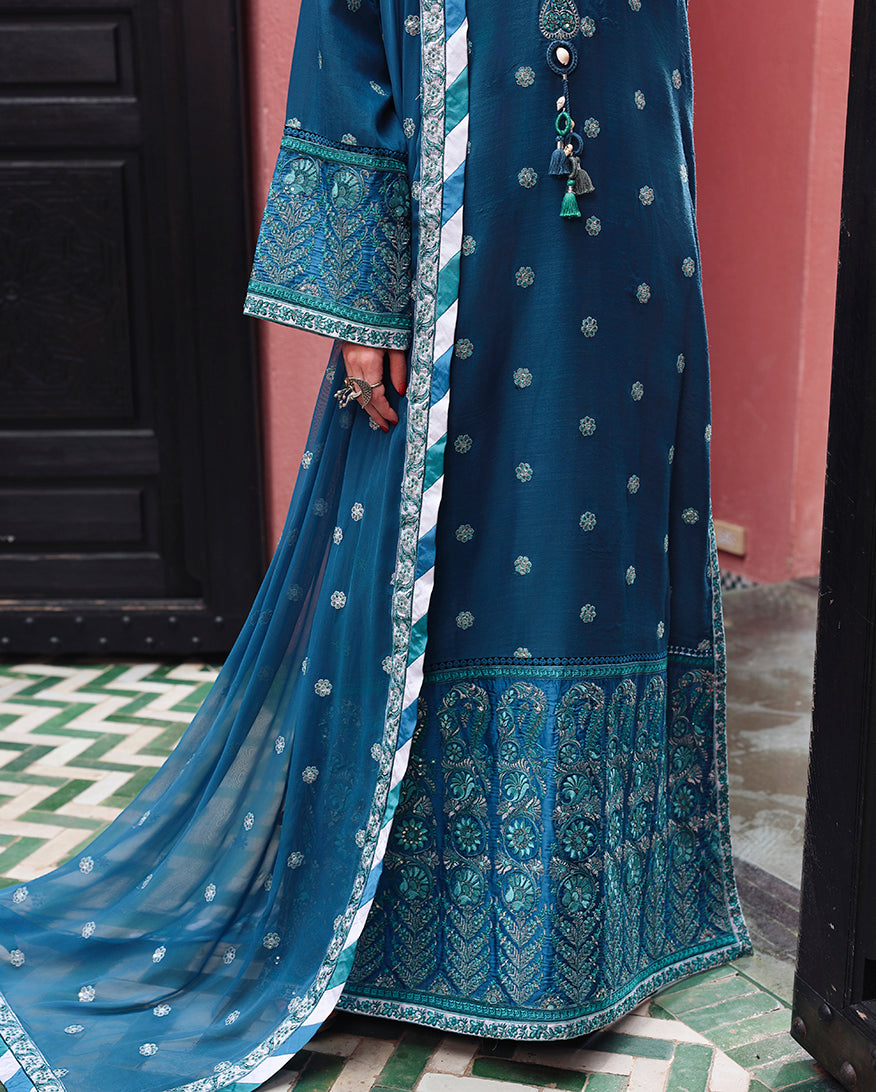 Close-up of embroidered daaman border and sequinned hem detail on teal raw silk shirt