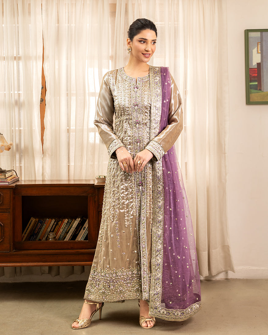 Woman wearing golden beige embellished lama silk suit, front standing by sheer curtains