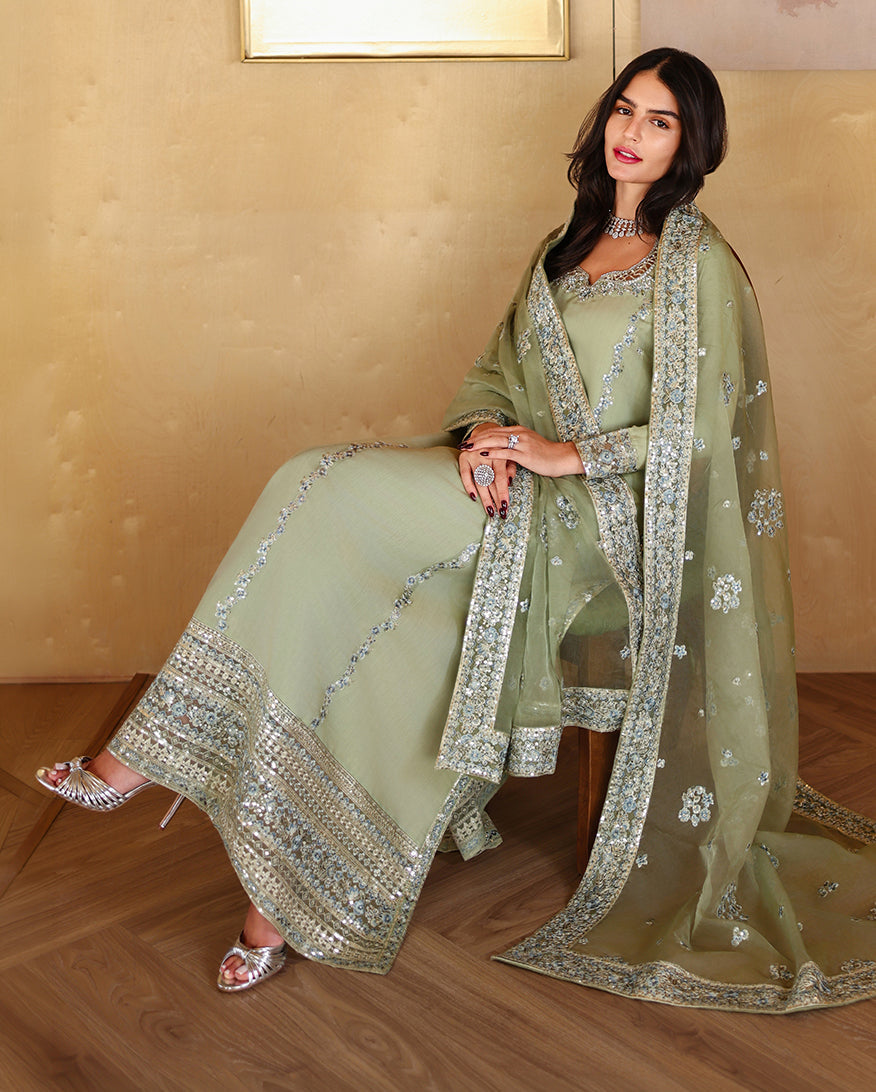 Seated styled shot of sage green luxury pret suit with embroidered hem, Zarminay collection