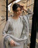 Woman wearing grey embroidered raw silk suit with diagonal color-blocked border under stone archway