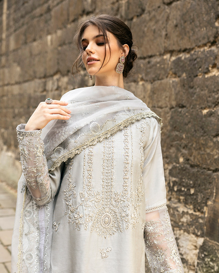 Woman wearing grey embroidered raw silk suit with diagonal color-blocked border under stone archway